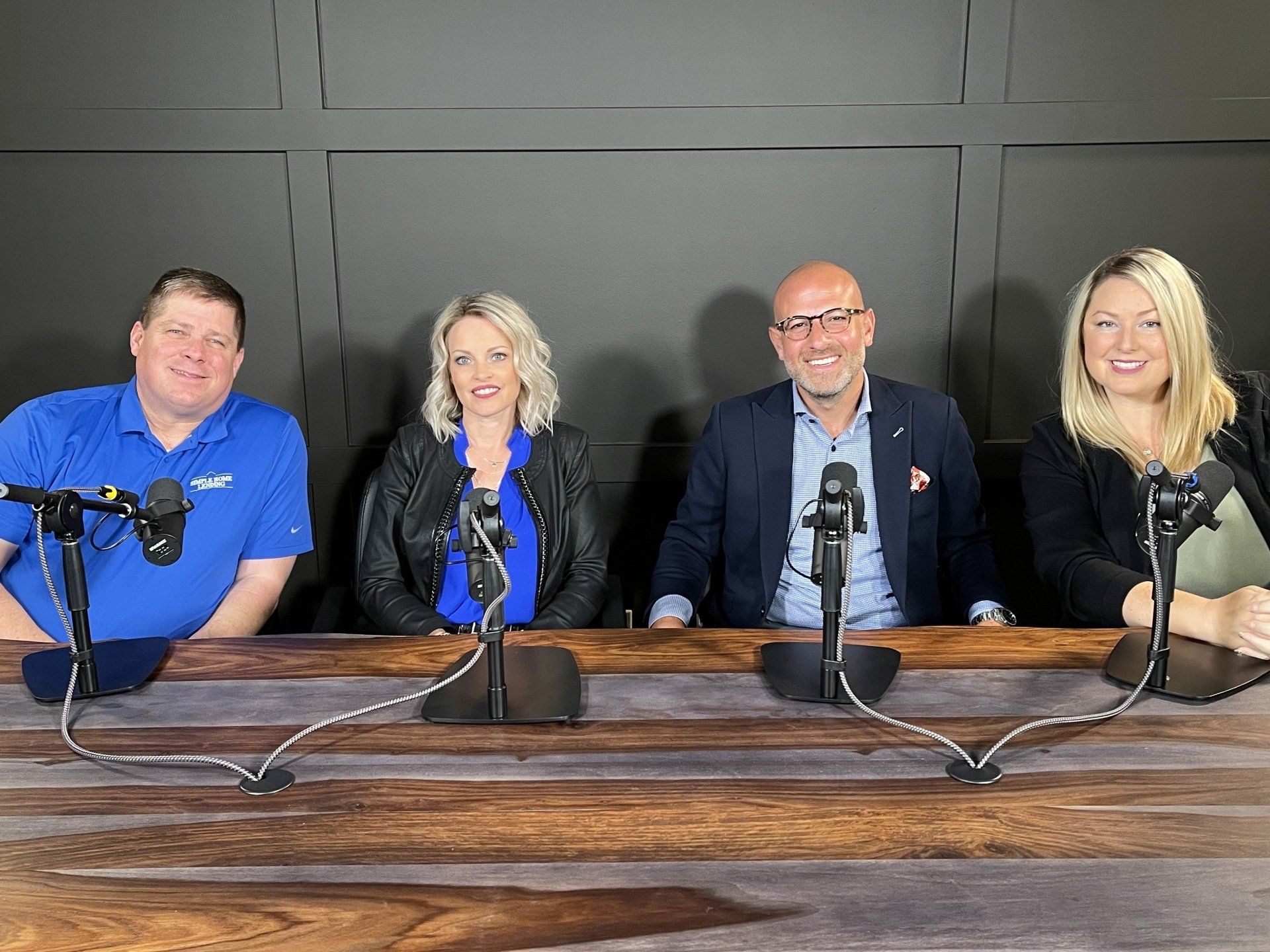 Four people seated at a podcast table with microphones in a studio setting