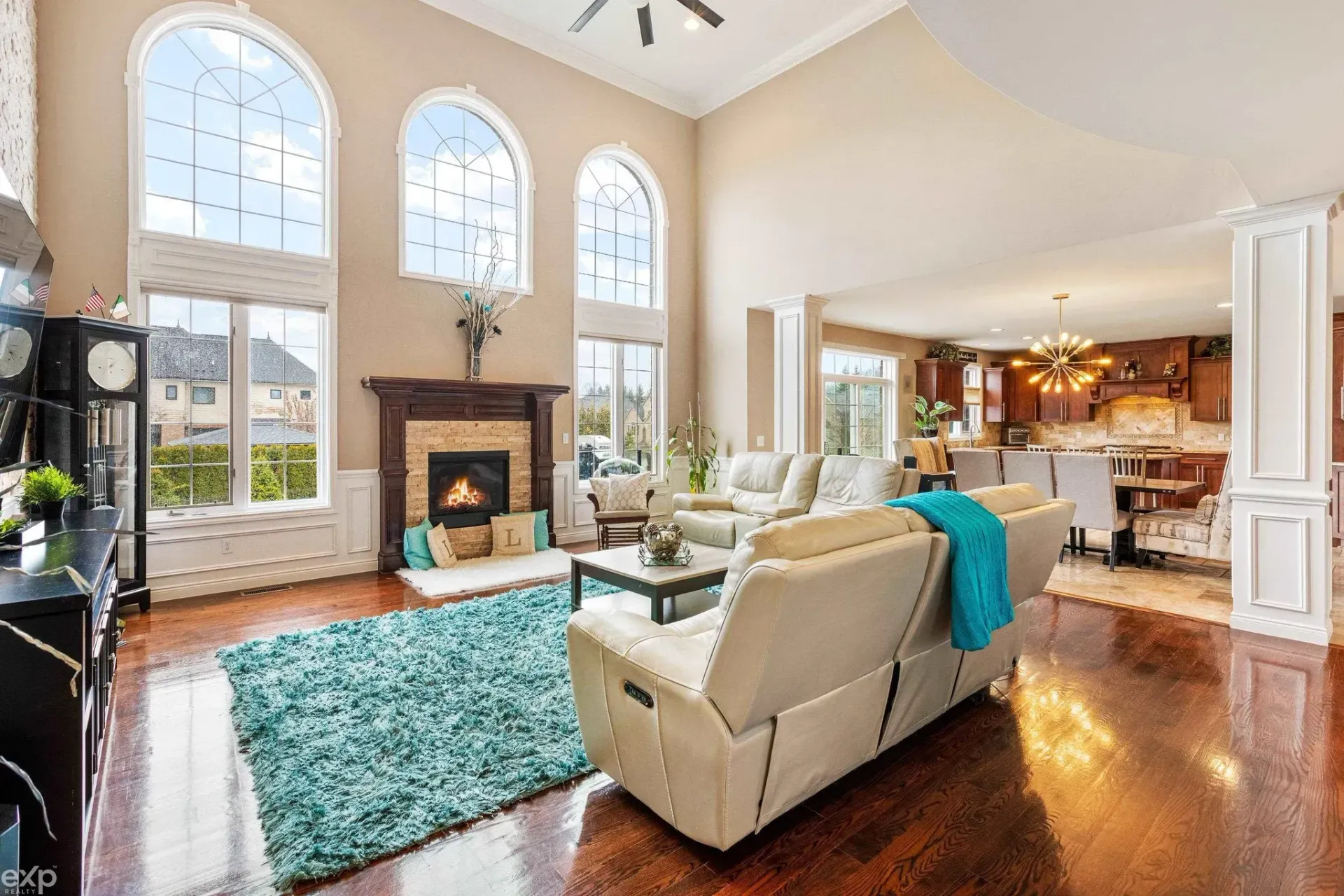 Bright living room with tall arched windows, fireplace, white sofas, and a turquoise rug on hardwood floors.