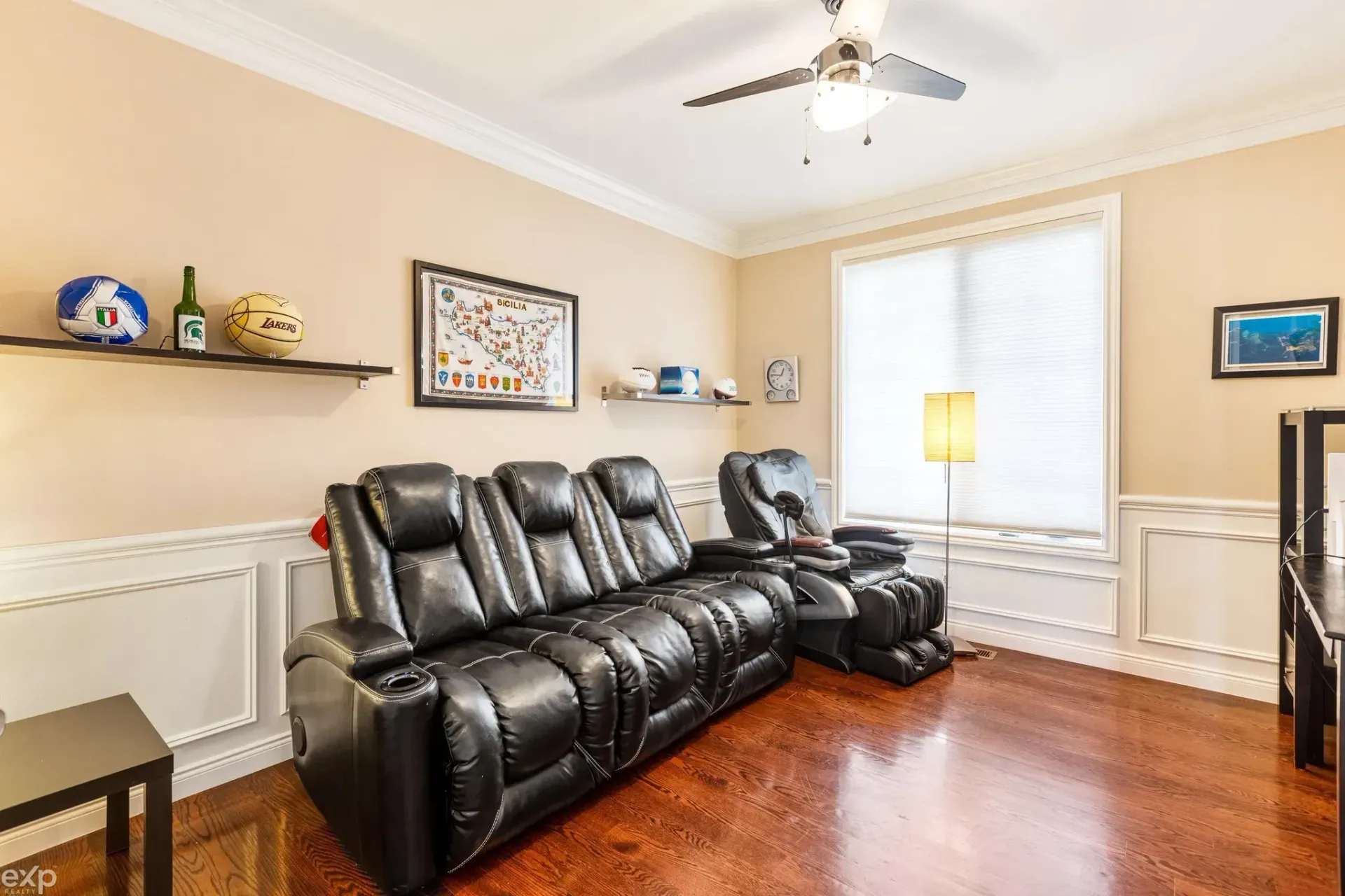 Bright living room with black leather sofa, hardwood floor, wall shelves, and a large window with a lamp