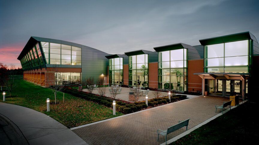 Modern glass office building with illuminated windows and landscaped courtyard at dusk