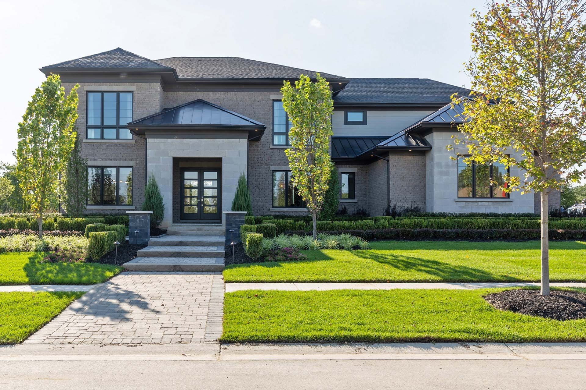 Large modern two-story house with stone facade, manicured lawn, and front walkway in bright daylight