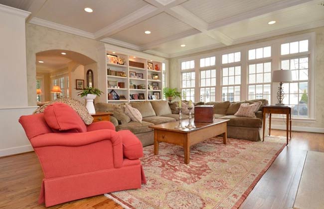 Bright living room with coral armchair, beige sofa, wood coffee table, built-in shelves, and large windows