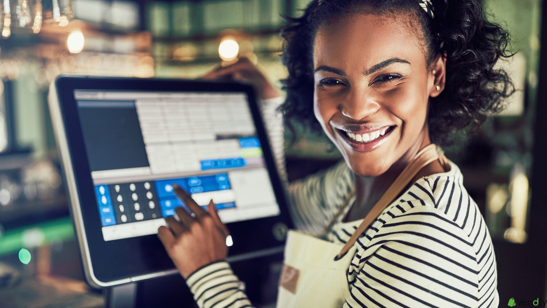 Empleada sonriente usando una pantalla táctil de punto de venta (POS) en un restaurante o café.