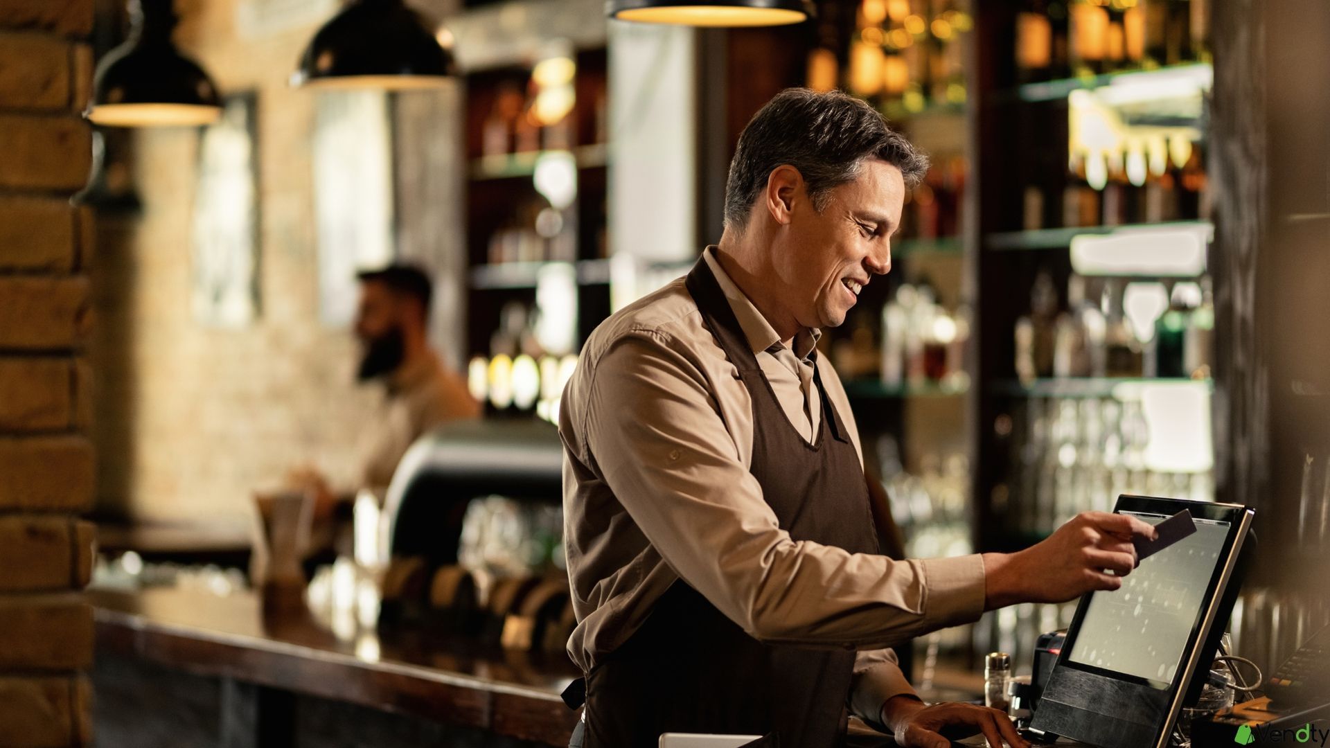 Mesero sonriente usando sistema POS en la barra de un restaurante elegante.