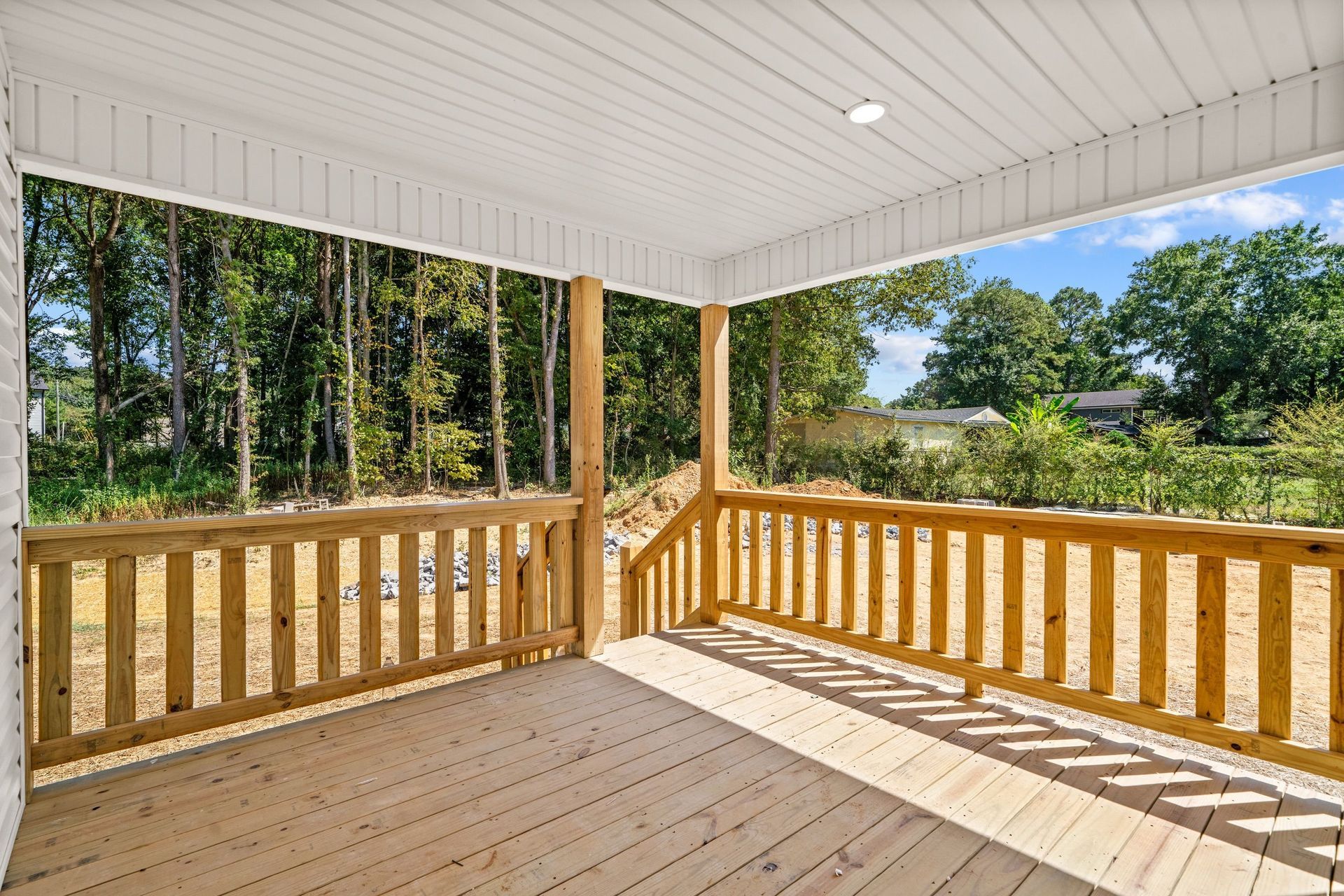 Covered wooden porch with railings overlooking a wooded yard on a sunny day