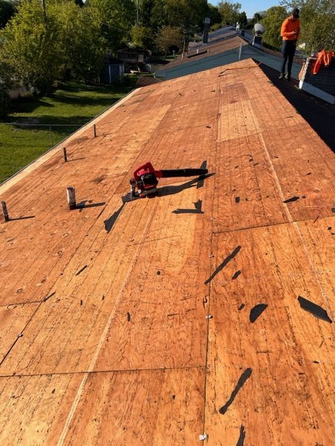 A person using a yellow pneumatic nail gun to install asphalt shingles on a roof.
