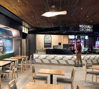 Modern café seating area with tables and chairs, a counter, and “Nisqually Grounds” signage