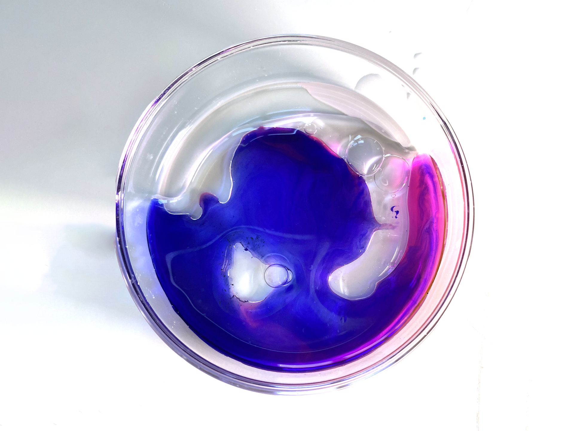 Glass bowl with swirling blue and pink liquid on a white background