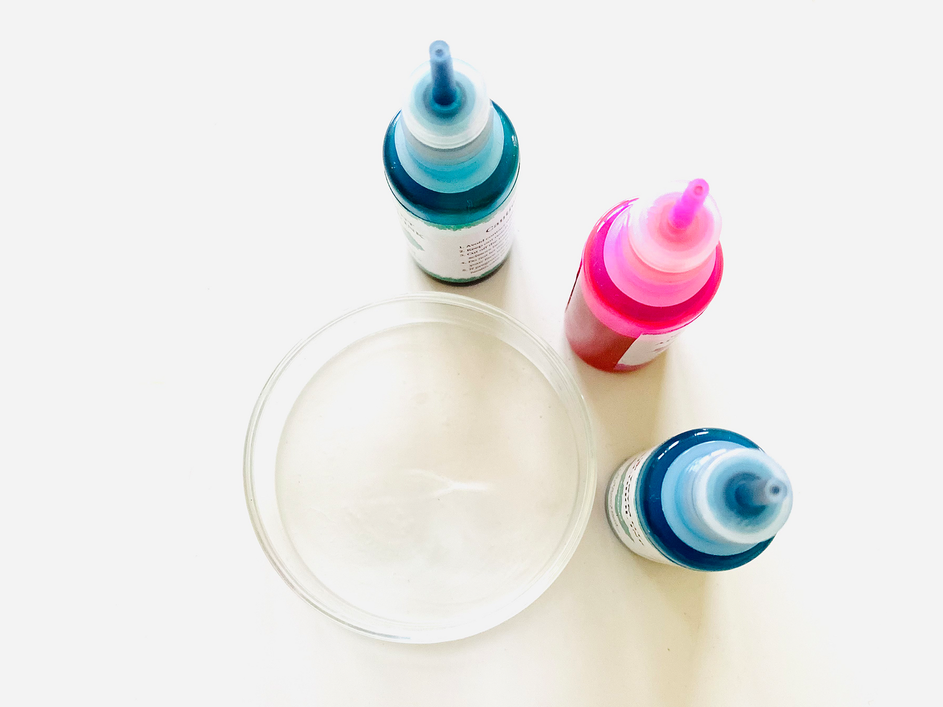 Three colorful dropper bottles around a shallow bowl on a white background