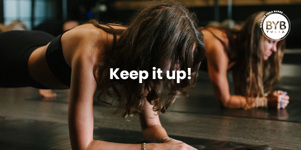 Two people in a dimly lit studio perform a forearm plank on yoga mats with the text