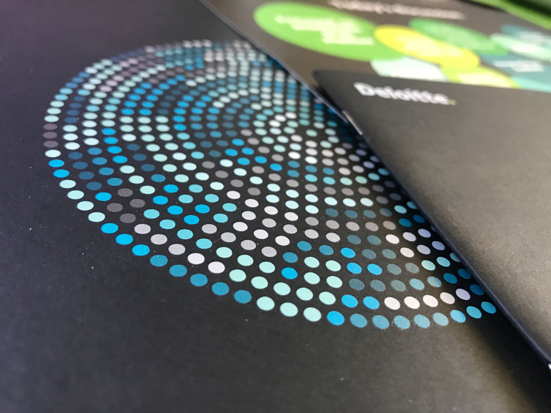 A close-up of a black brochure featuring a Deloitte logo and a pattern of blue and grey dots arranged in a spiral.