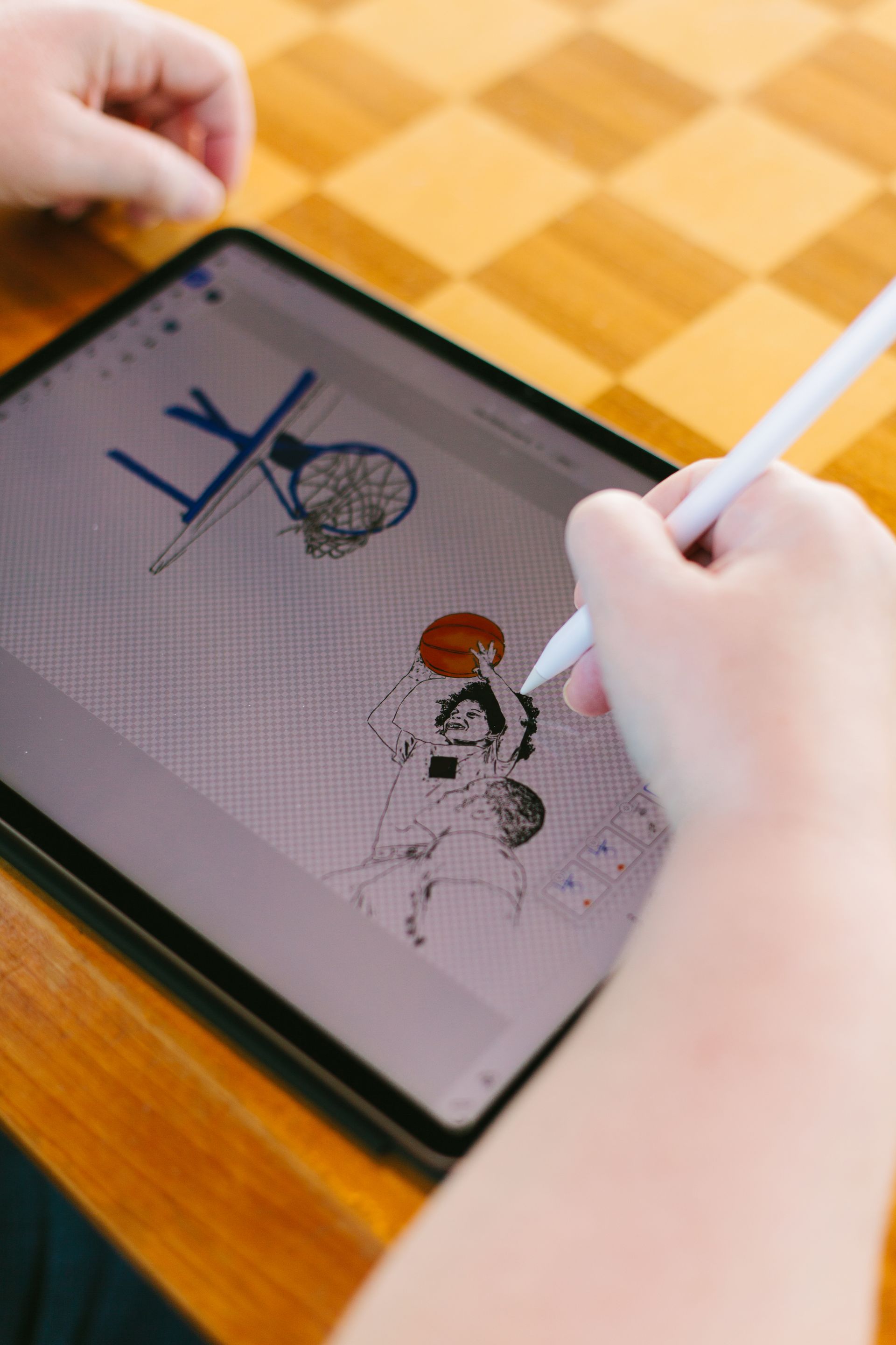 Hands using a stylus to draw on a tablet with a sketch on screen