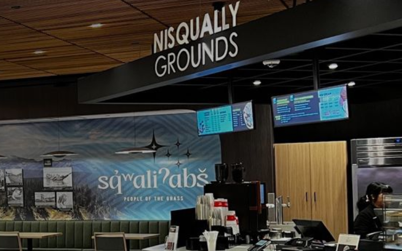 Nisqually Grounds coffee kiosk with black sign, menu screens, and a blue “squali’abs” backdrop