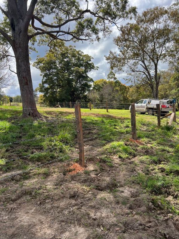 A Wooden Barbed Fence is Surrounded by Grass and Trees in a Field — Aztech Fencing In Upsalls Creek, NSW