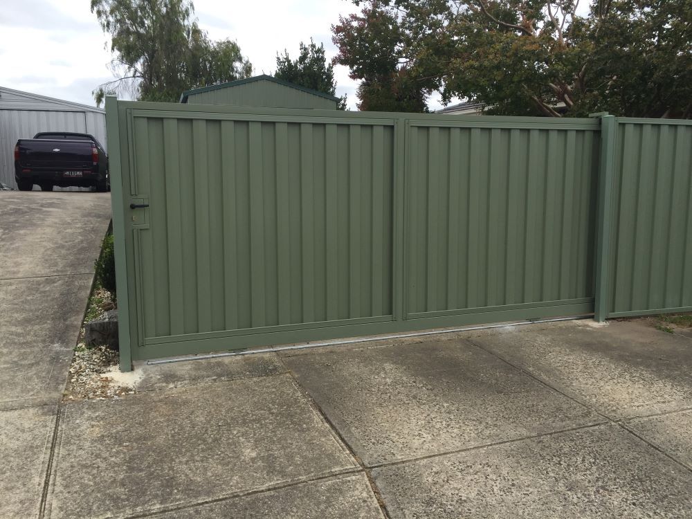 A Green Fence With a Black Car Parked Behind It — Aztech Fencing In Laurieton, NSW