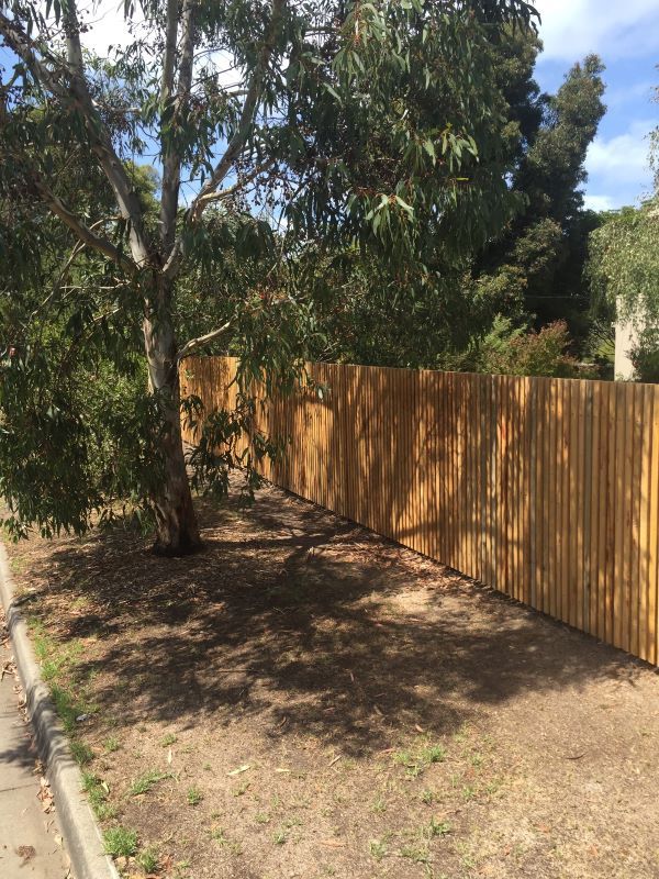 A Wooden Fence is Surrounded by Trees in a Yard — Aztech Fencing In Kew, NSW