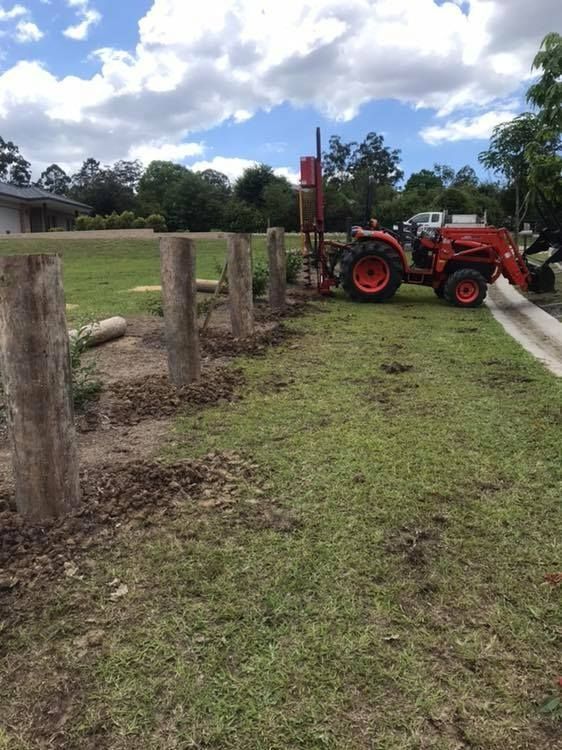 A Red Tractor is Working on Installing a Fence in a Grassy Field — Aztech Fencing In Upsalls Creek, NSW