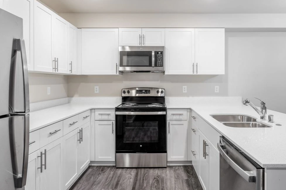Bright white modern kitchen with stainless steel appliances and gray backsplash, viewed from the center.