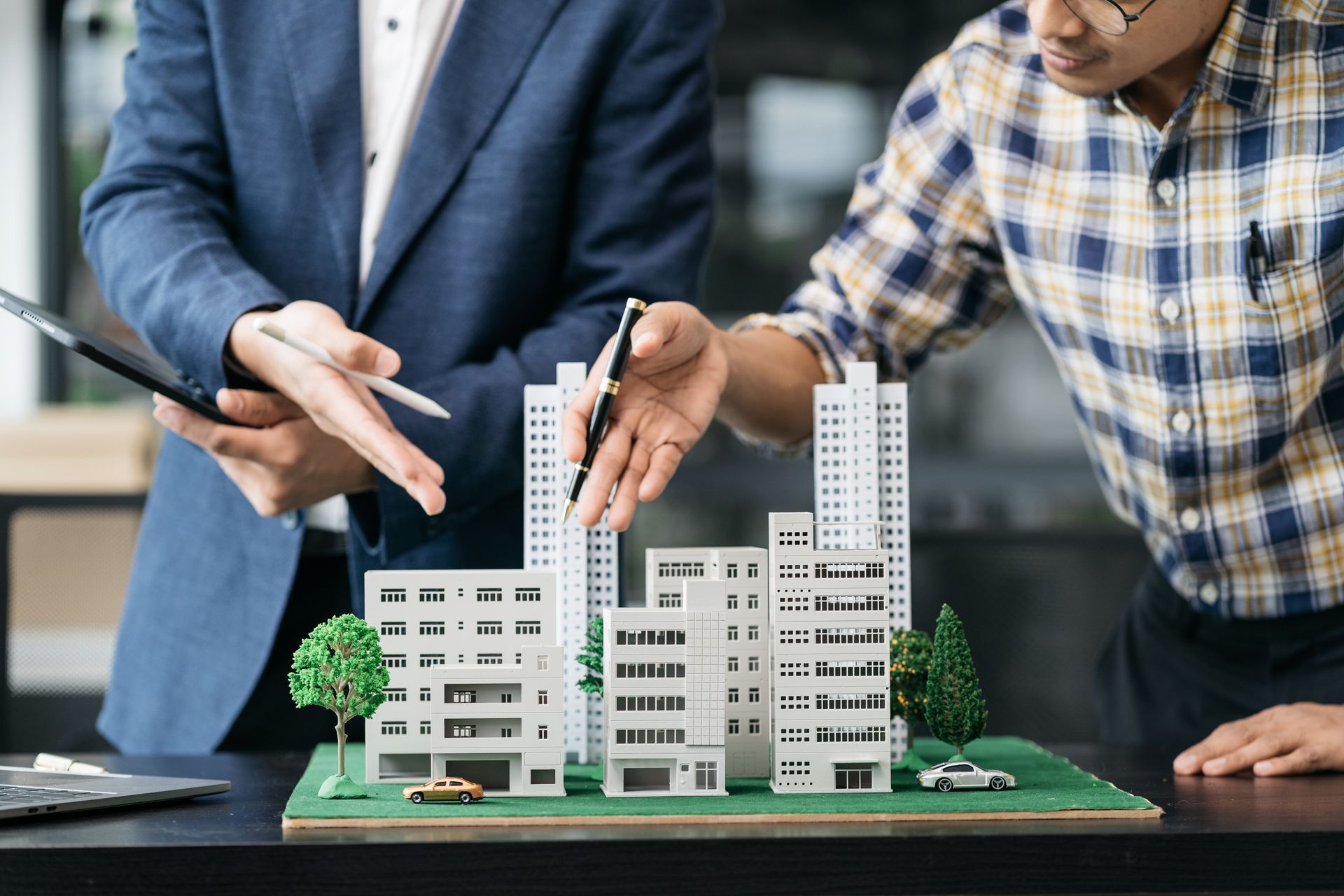 Two people pointing at an architectural scale model of a building complex on a table