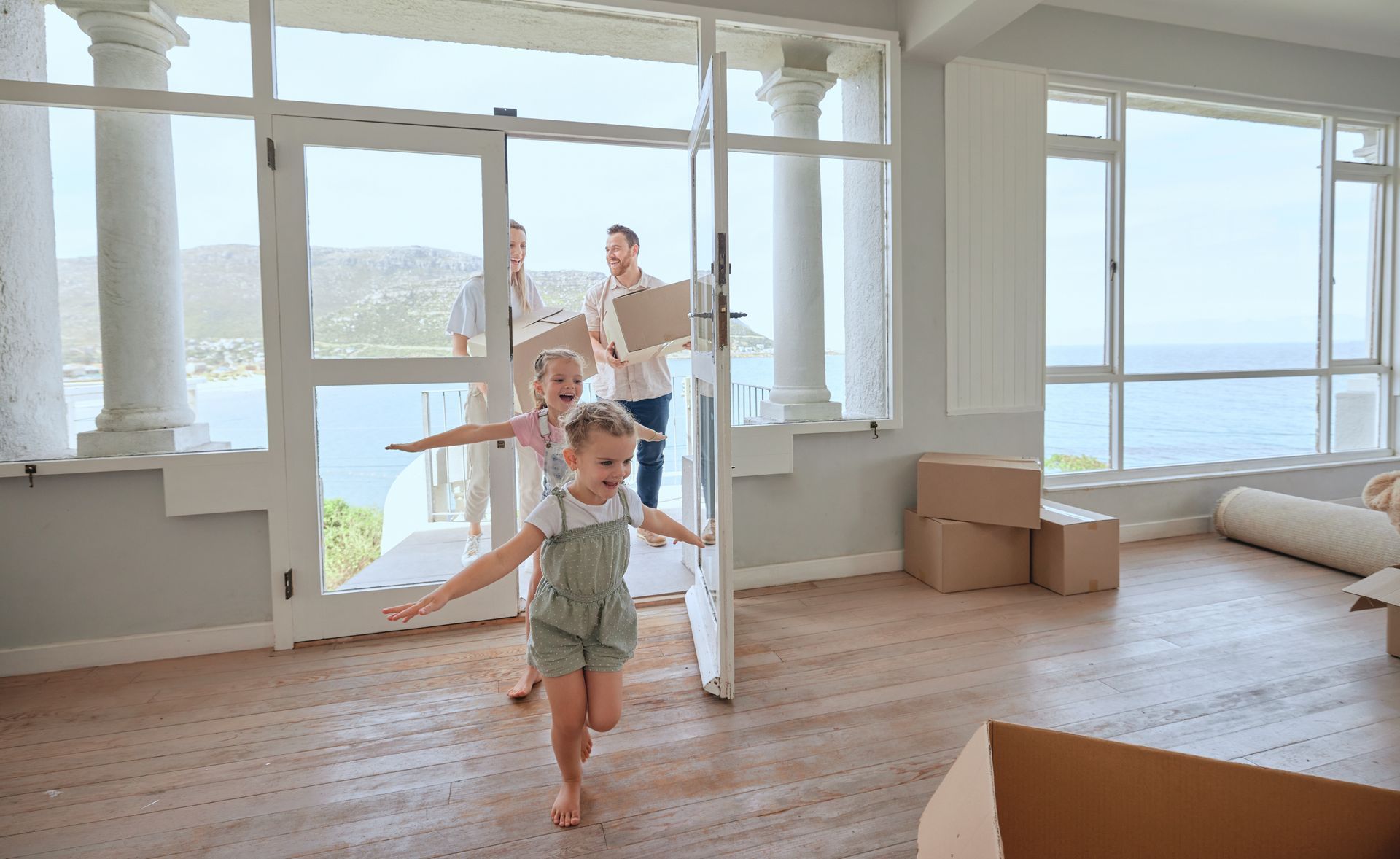 Child running in a bright seaside room with a man behind and boxes on the floor