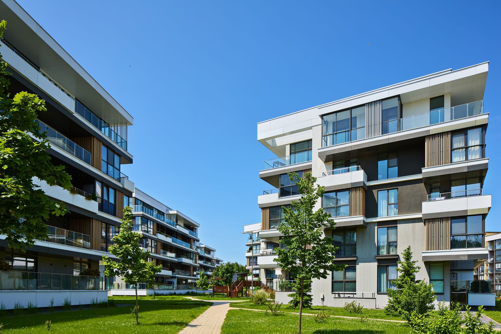 Modern apartment buildings with balconies and a green courtyard under a clear blue sky