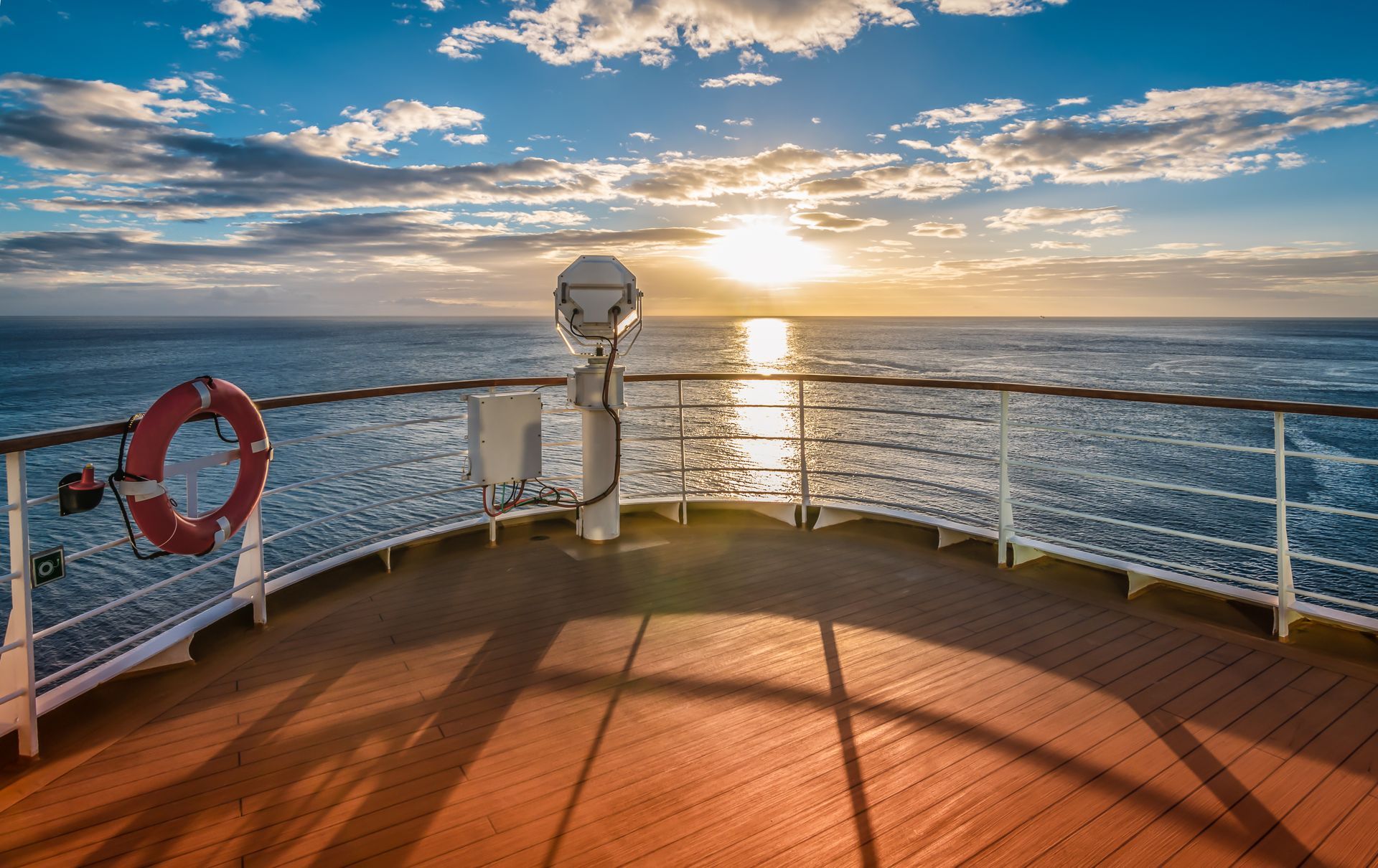 The deck of a cruise ship at sunset, overlooking the calm blue ocean with a life ring mounted on the railing. The deck of a cruise ship at sunset, overlooking the calm blue ocean with a life ring mounted on the railing.