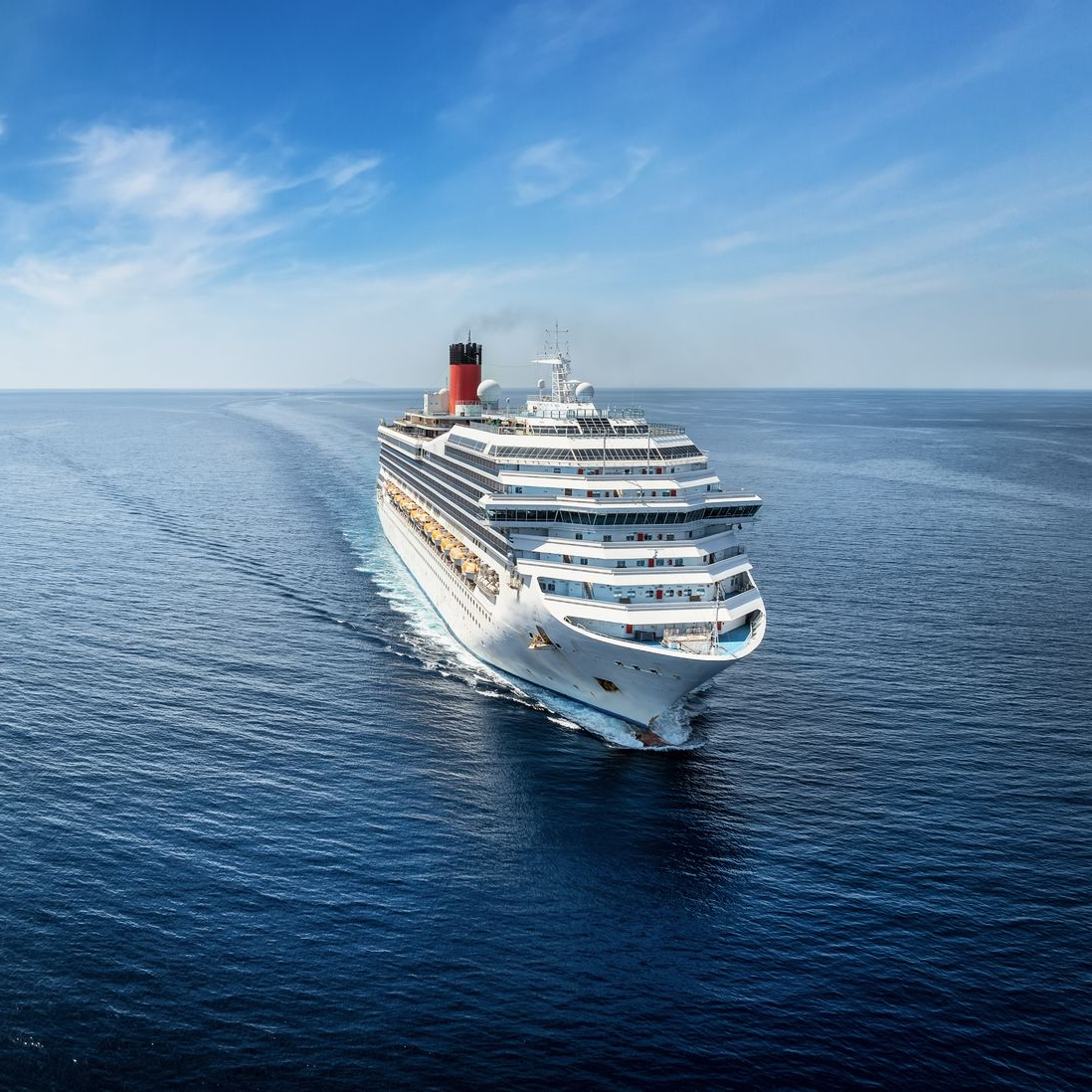 A large cruise ship sails across a vast, calm ocean under a bright, clear blue sky. A large cruise ship sails across a vast, calm ocean under a bright, clear blue sky.