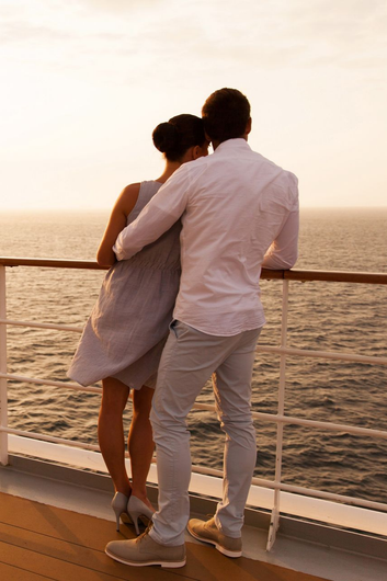 A couple stands at the railing of a cruise ship, watching the sunset over the ocean. A couple stands at the railing of a cruise ship, watching the sunset over the ocean.