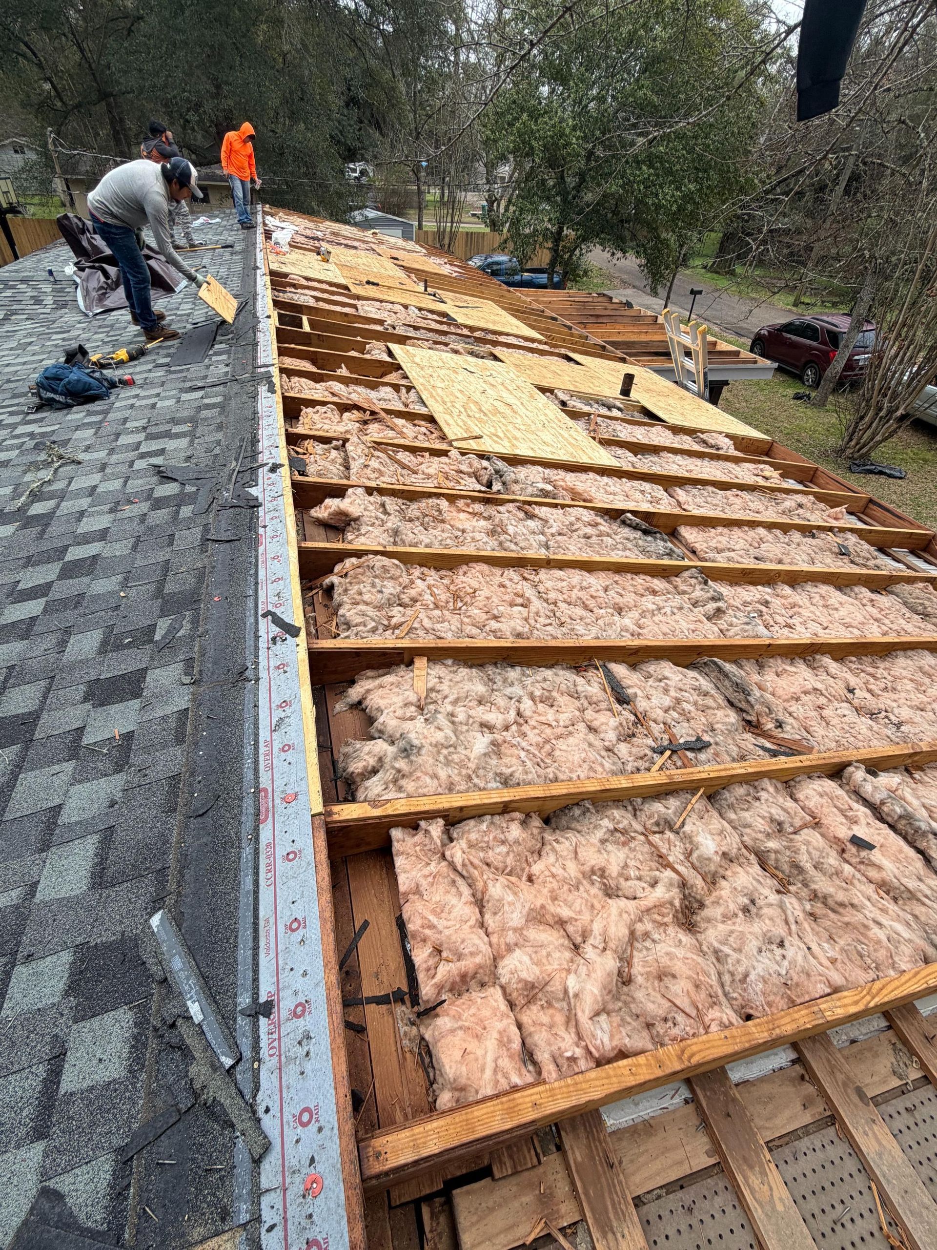 Workers installing roof insulation and wood framing on a house under construction