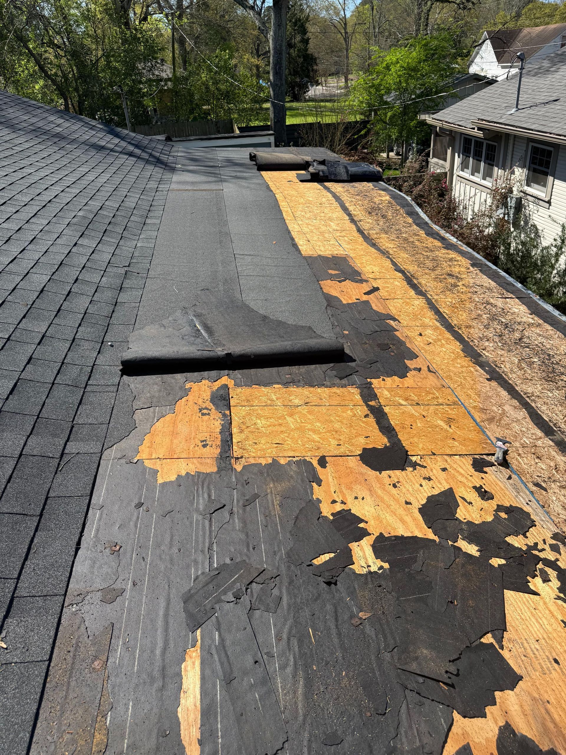 Damaged roof with torn black shingles exposing orange underlayment and a raised patch near the ridge