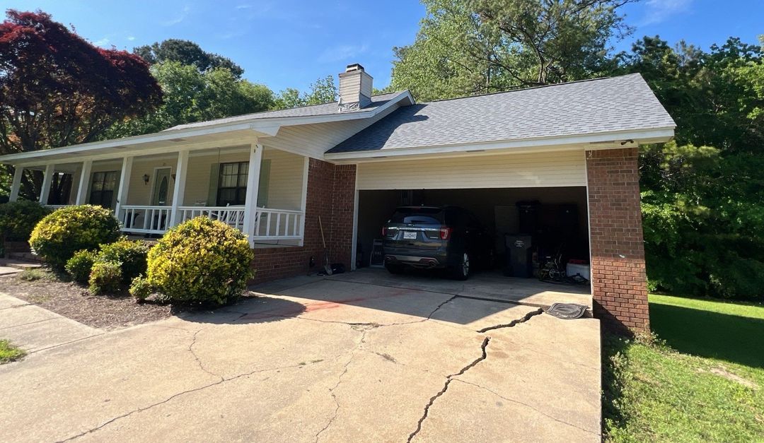 Brick ranch house with attached carport, driveway, and parked car on a sunny day