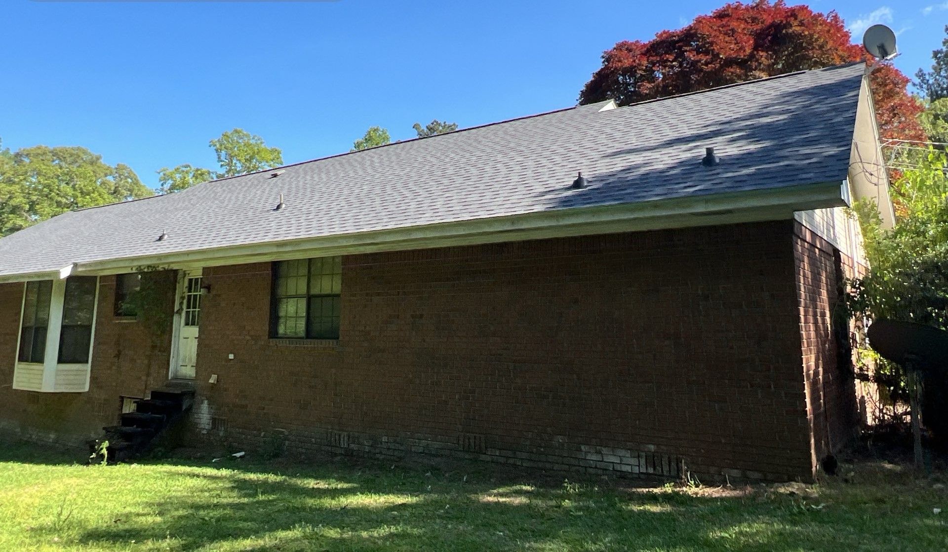 Single-story brick house with a gray shingle roof and green lawn in bright sunlight