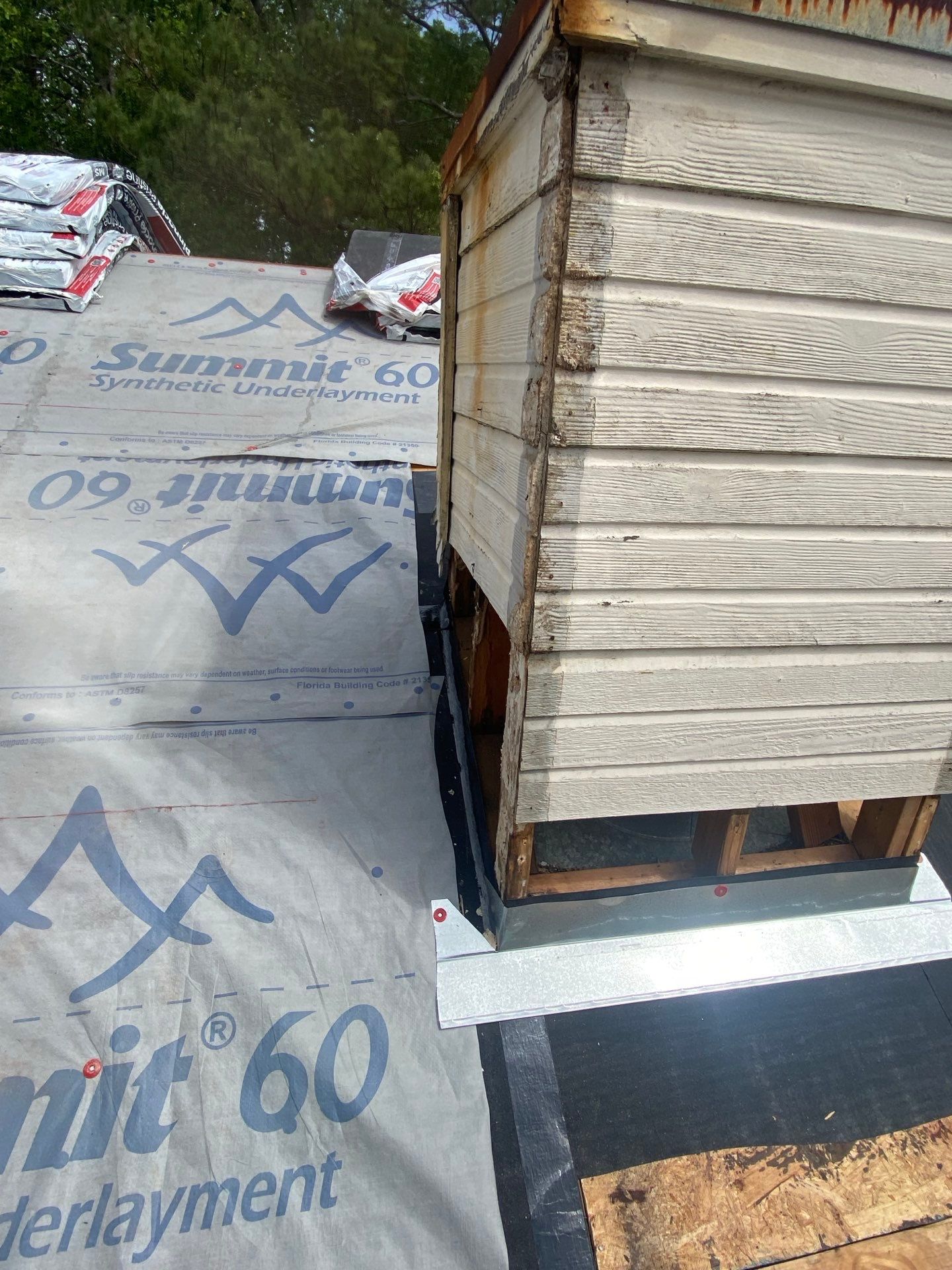 Stacked wood pallets on a rooftop beside roofing underlayment rolls and a white membrane edge.