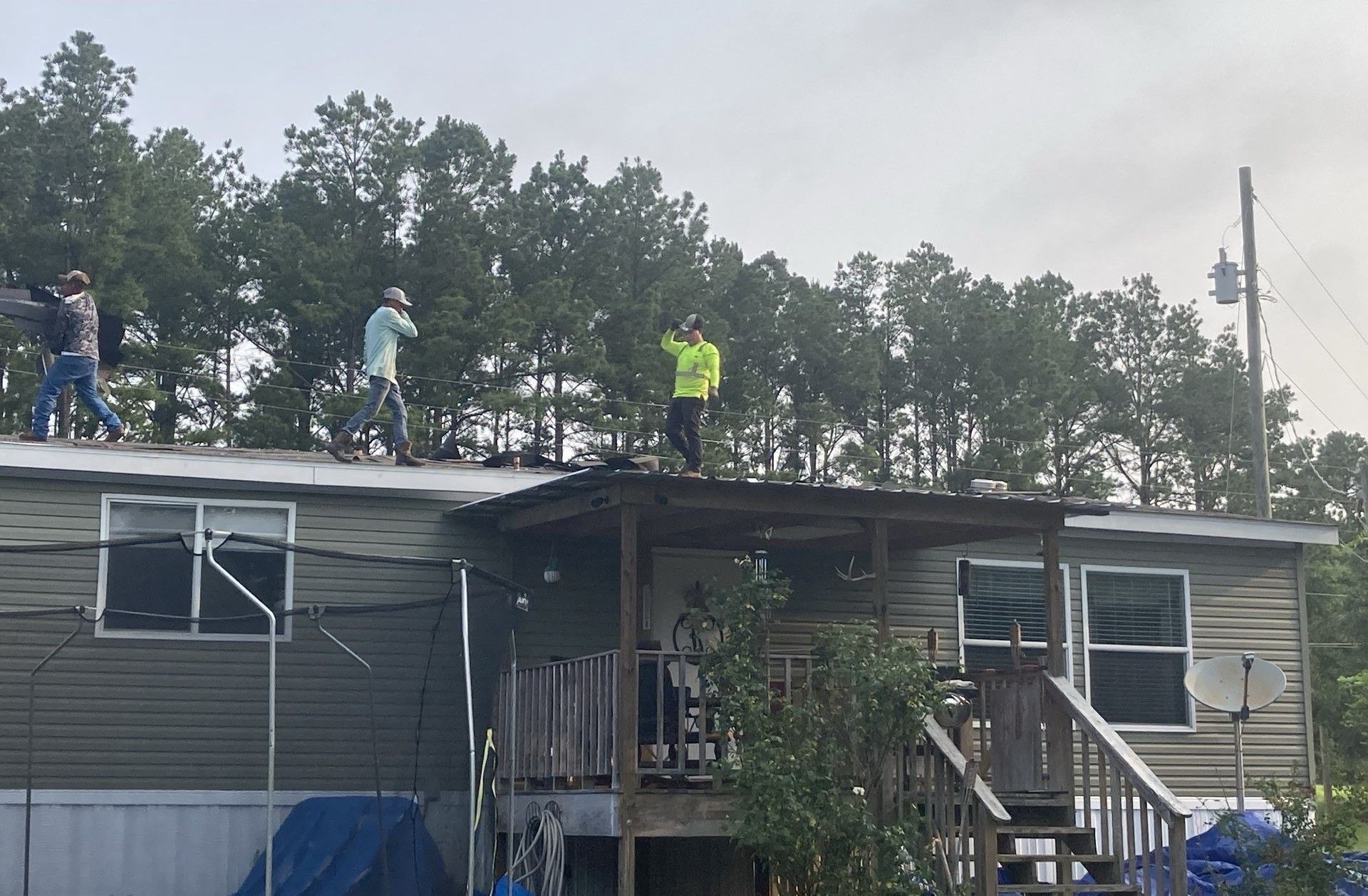 Workers on a damaged house roof, inspecting or repairing it after storm damage.