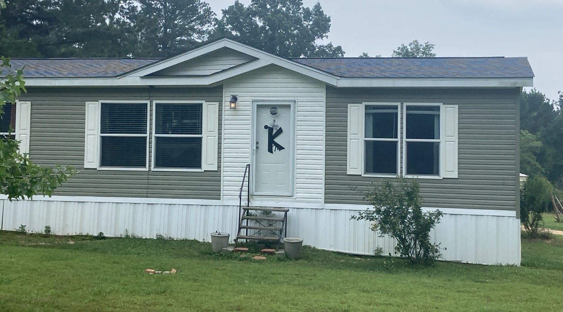 Small white house with green shutters, front steps, and a door marked with a black “K” flag.