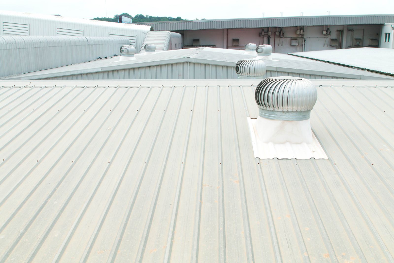 Rooftop with light gray metal panels and several silver ventilation fans under an overcast sky