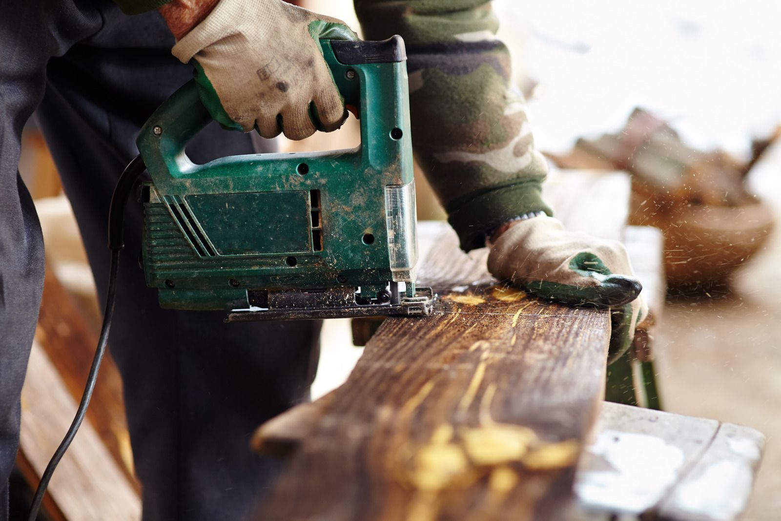 Person using a green power saw to cut a wooden plank outdoors