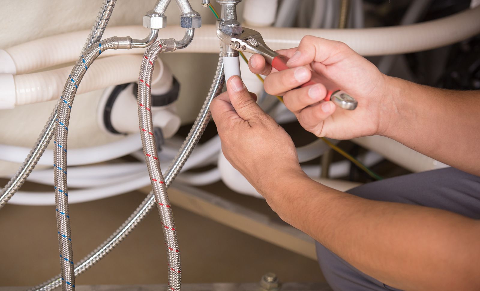 Hands tightening a braided metal hose connection under a sink cabinet