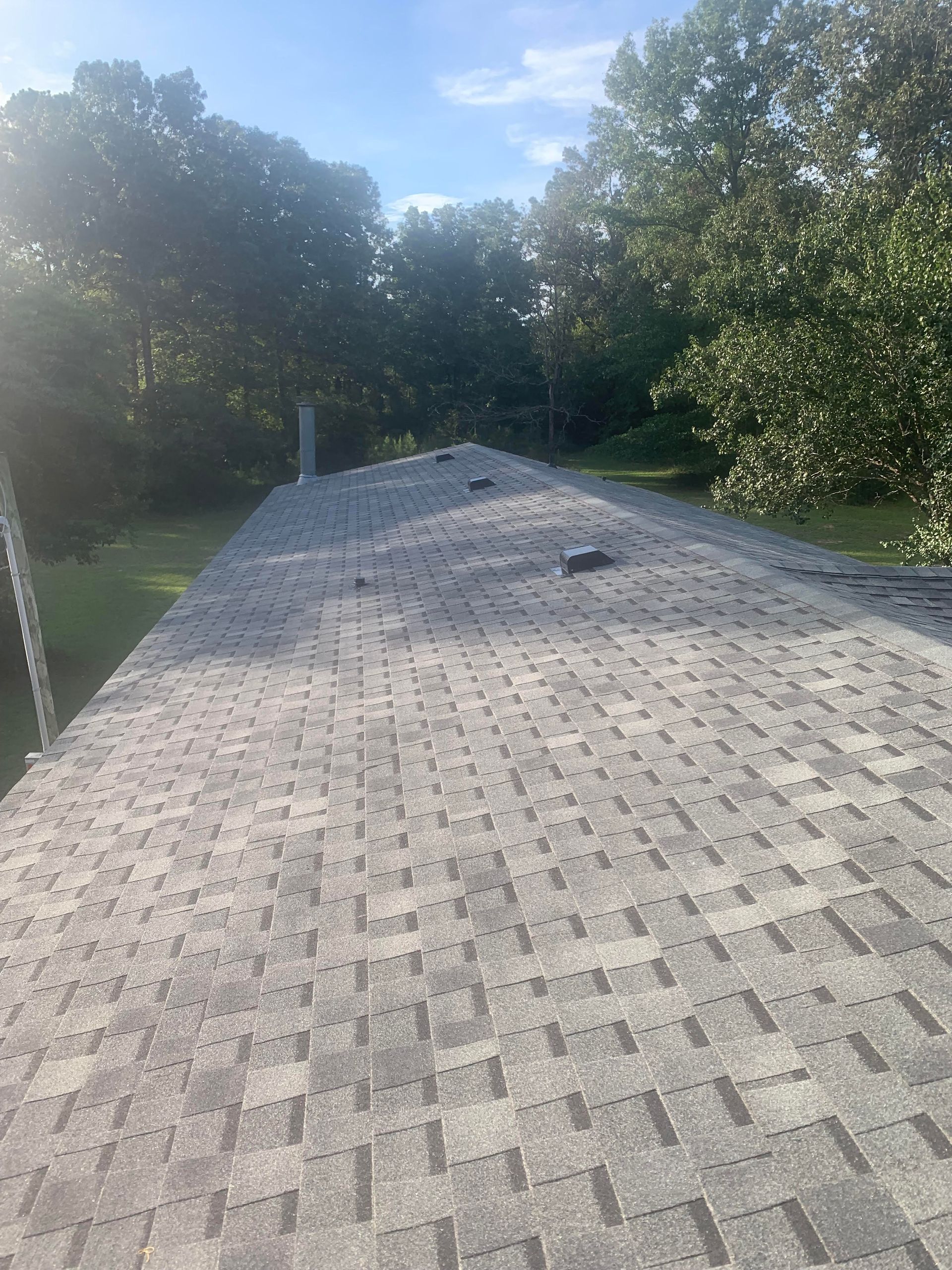 Gravel roof walkway with a small vent, surrounded by green trees under a blue sky