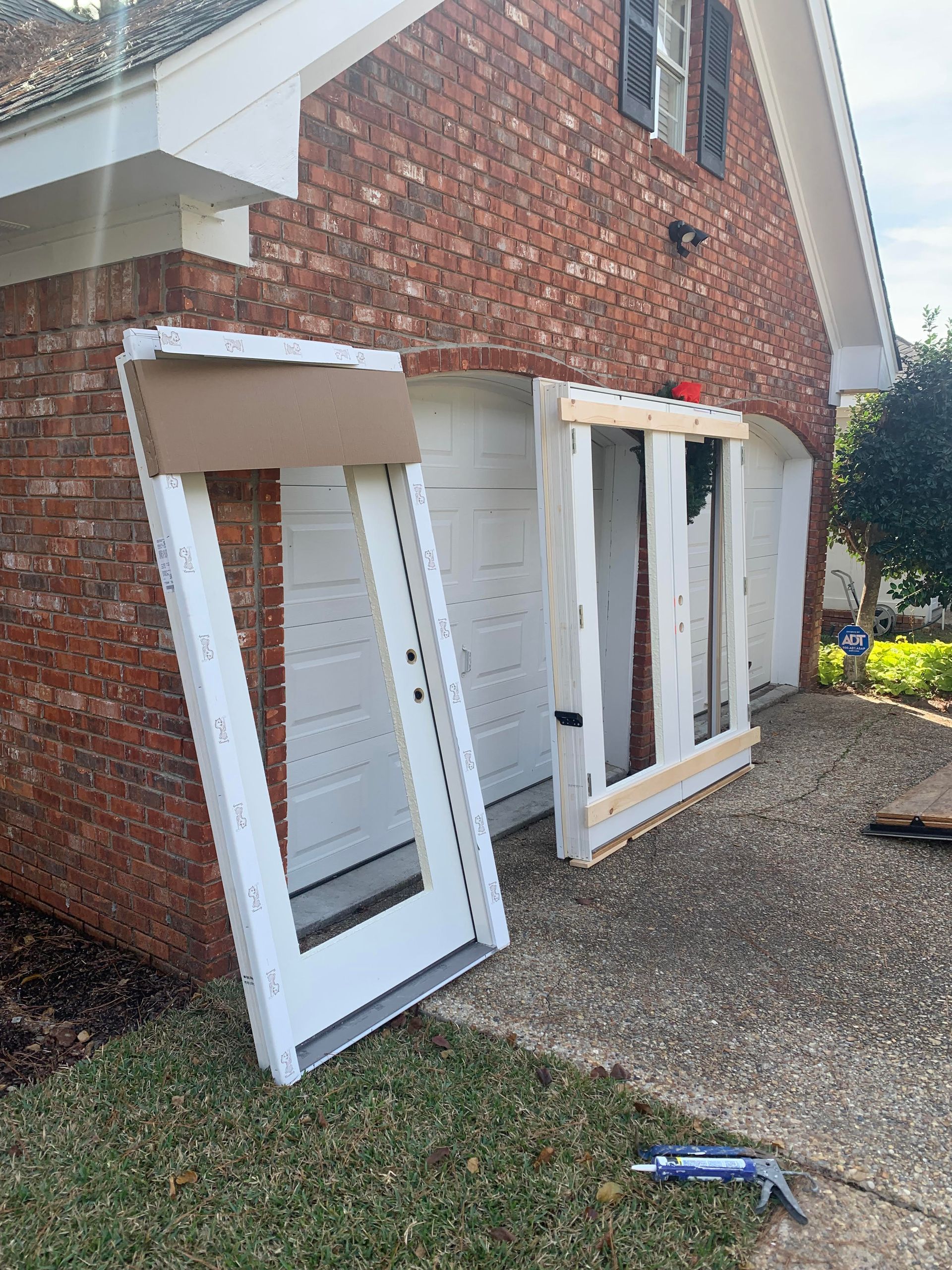 Broken white window frames leaning against a brick house exterior on a gravel path