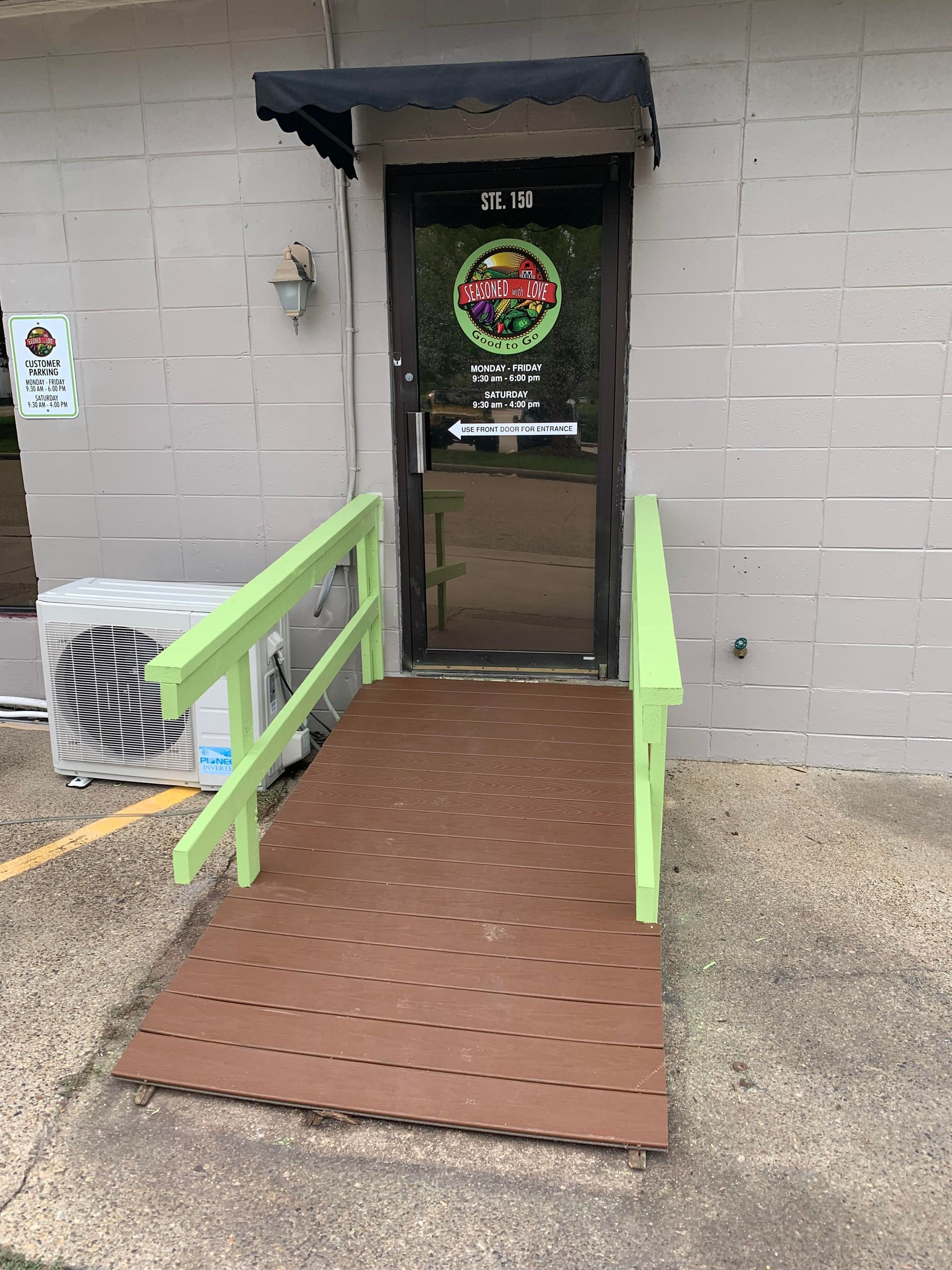 Entrance with a brown ramp, green handrails, and a glass door under a small awning.