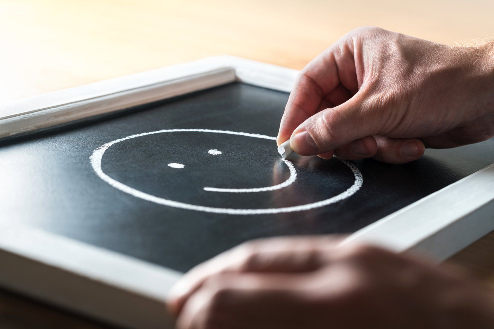 A person is drawing a smiley face on a blackboard.