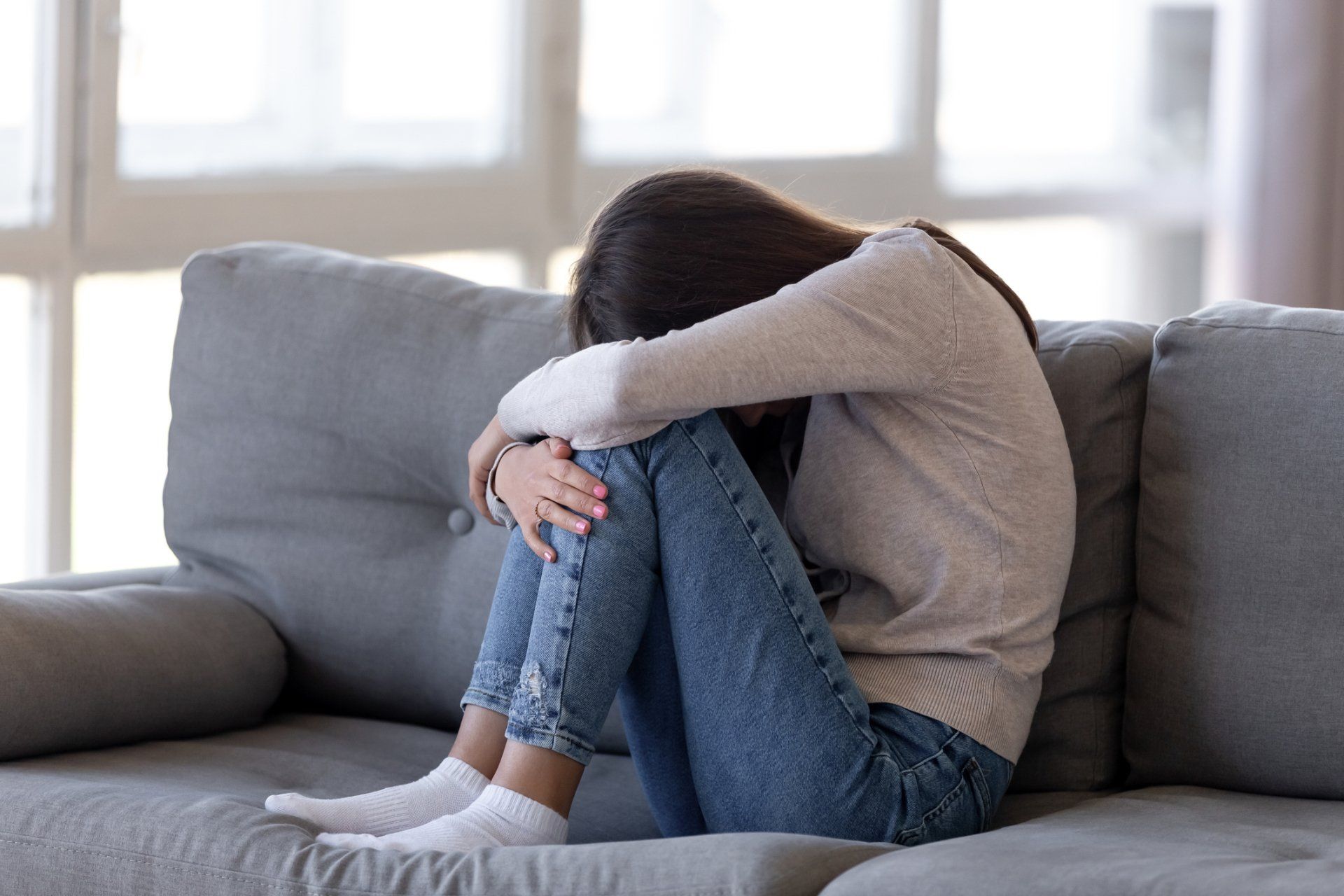 A woman is sitting on a couch with her head down.