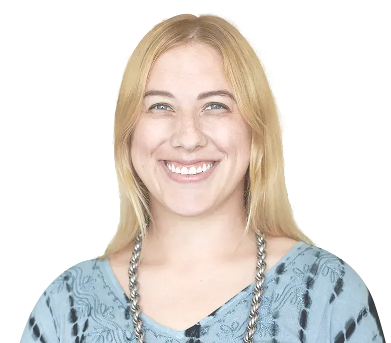 A smiling person with shoulder-length blonde hair, wearing a blue tie-dye shirt and a silver chain necklace.