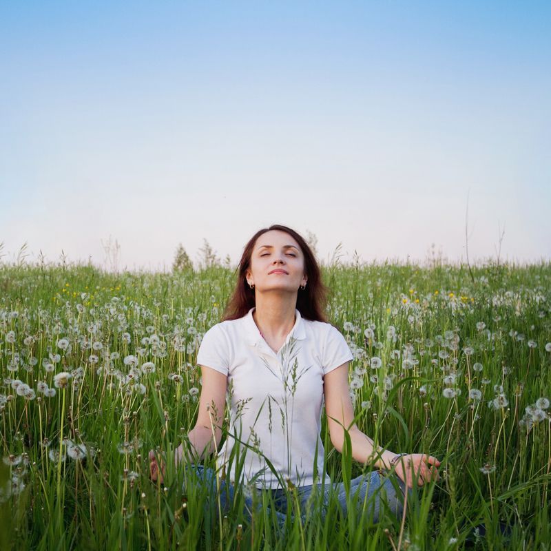 A woman is sitting in a lotus position in a field of dandelions.