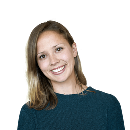 A person with shoulder-length hair wearing a dark teal sweater smiles against a plain white background.