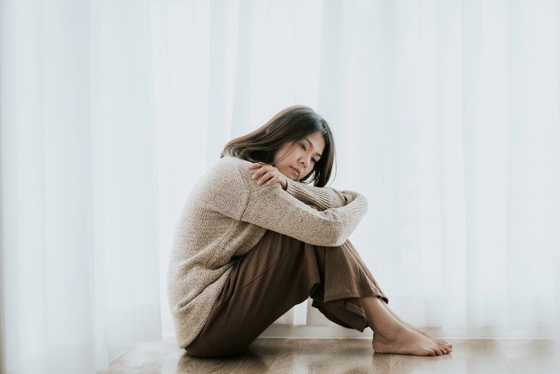 A woman is sitting on the floor in front of a window.