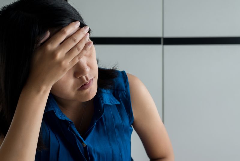 A woman is covering her face with her hand while sitting at a table.