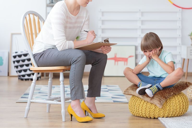 A woman is sitting in a chair talking to a young boy.