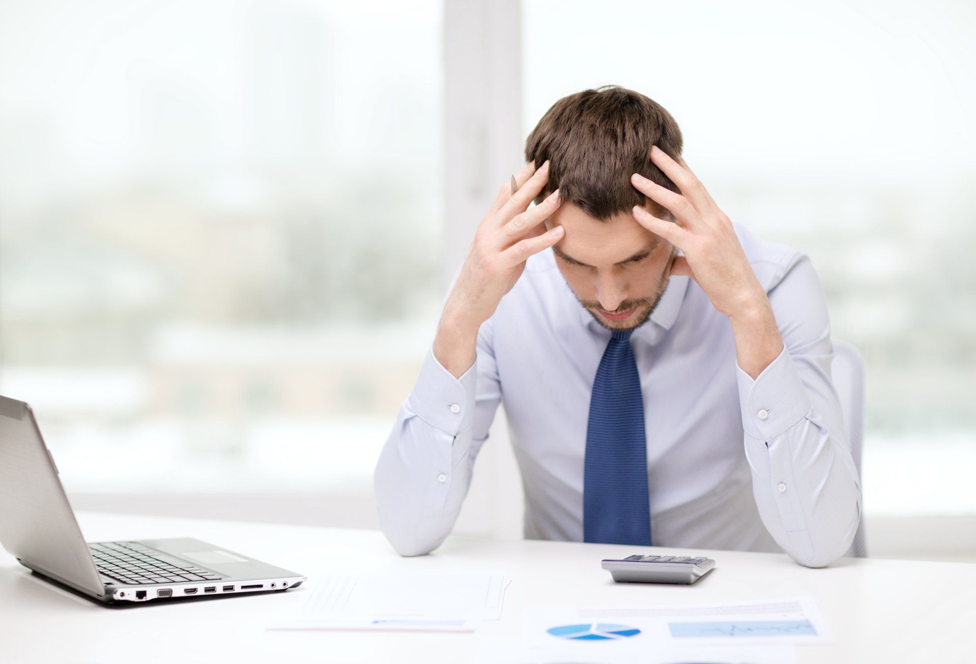 A man is sitting at a desk with his hands on his head.